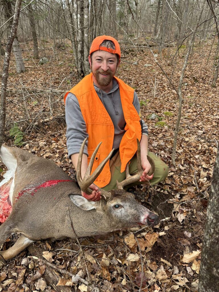 Hunter in blaze orange with a white-tailed buck on a guided Maine deer hunt