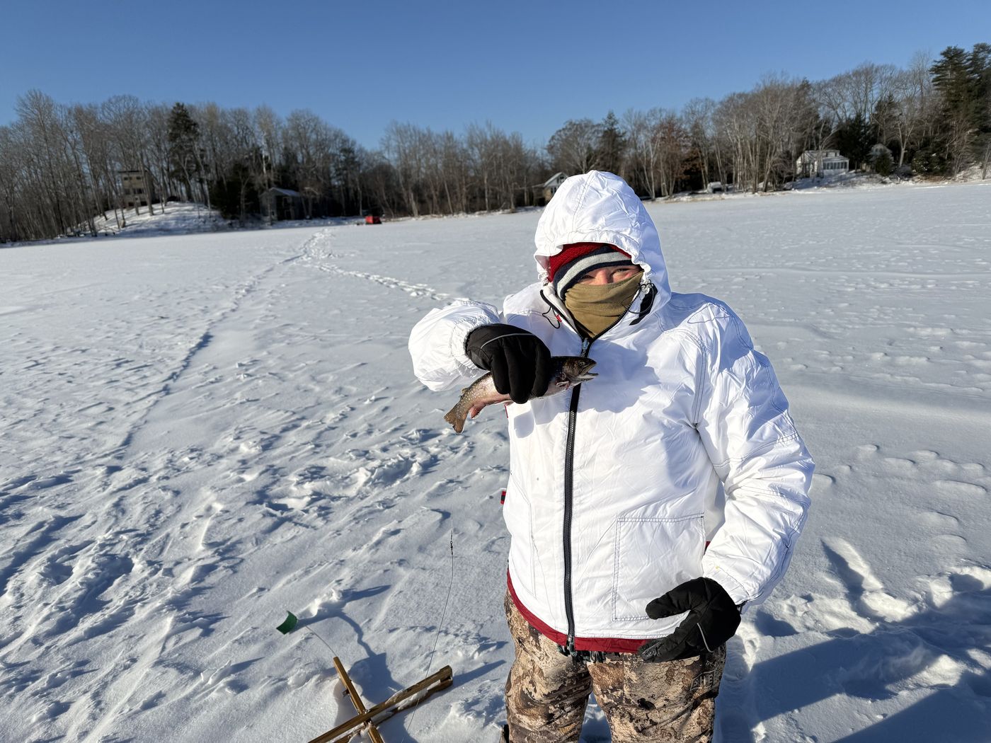 Angler holding a fish on a snow-covered Maine lake in winter