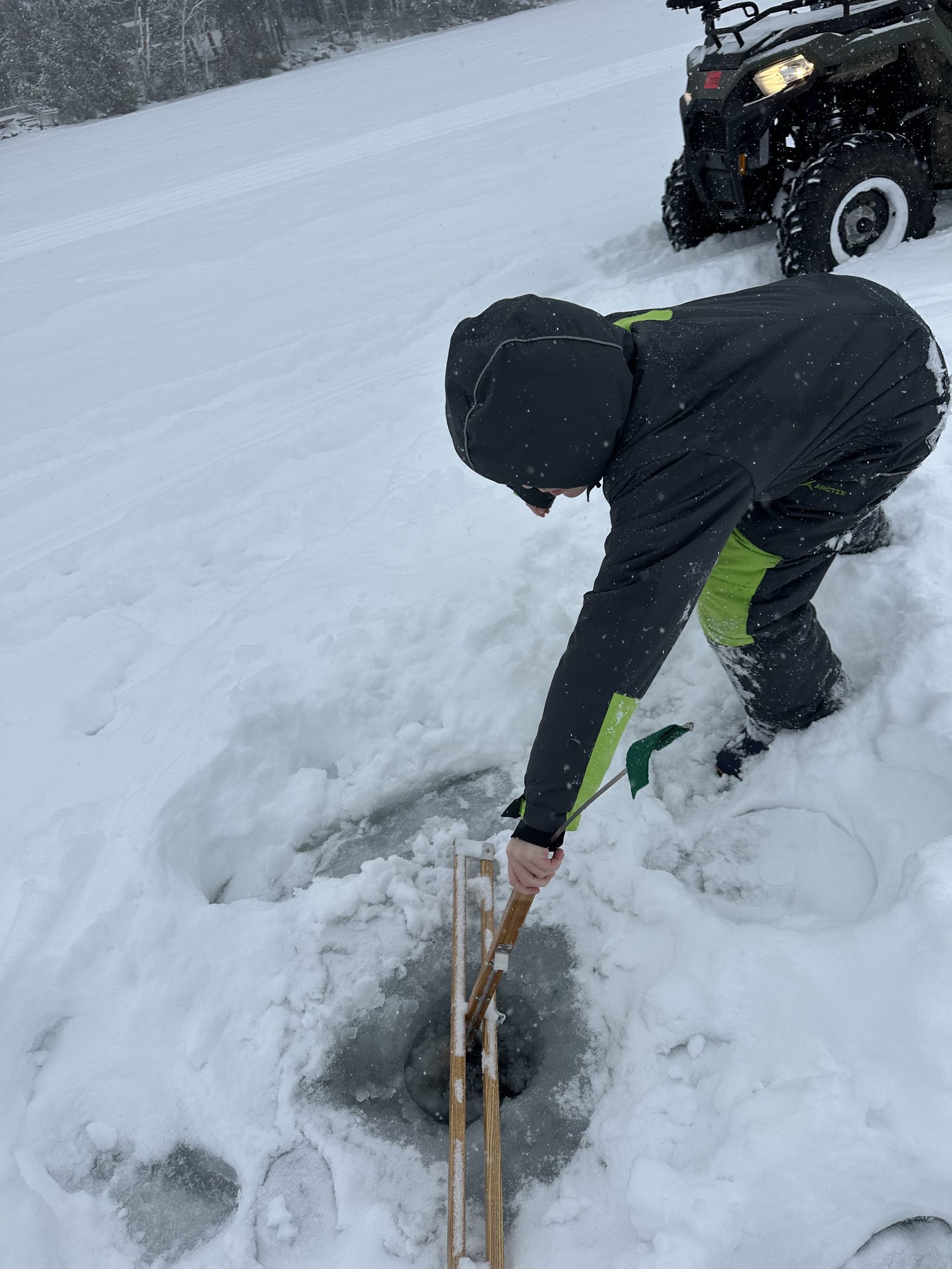 Drilling a hole with an ice auger on a frozen Maine lake