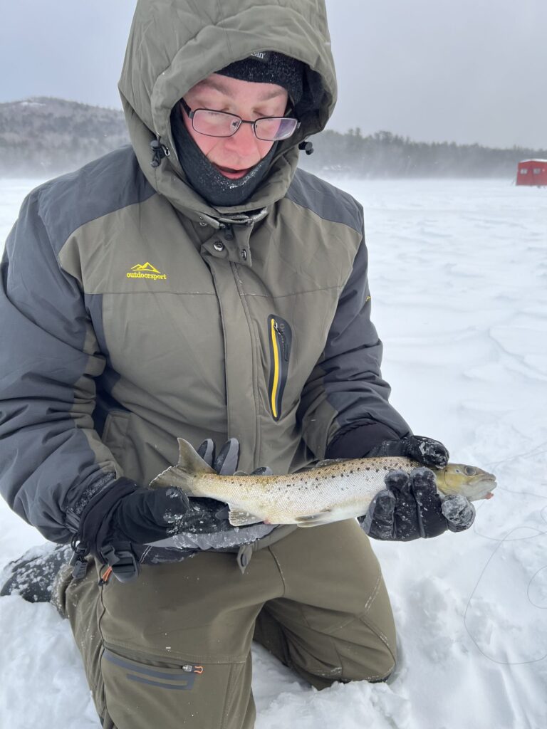 Angler on the ice holding a brown trout on a Maine guided ice fishing trip
