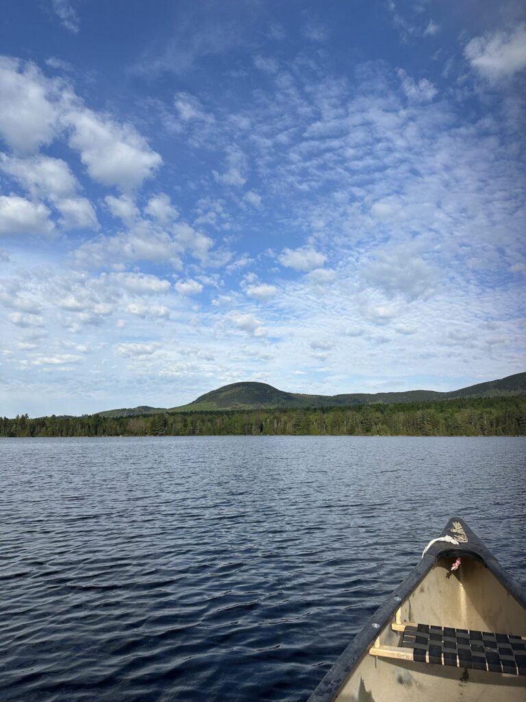 The bow of a canoe on a calm Maine lake under an open sky