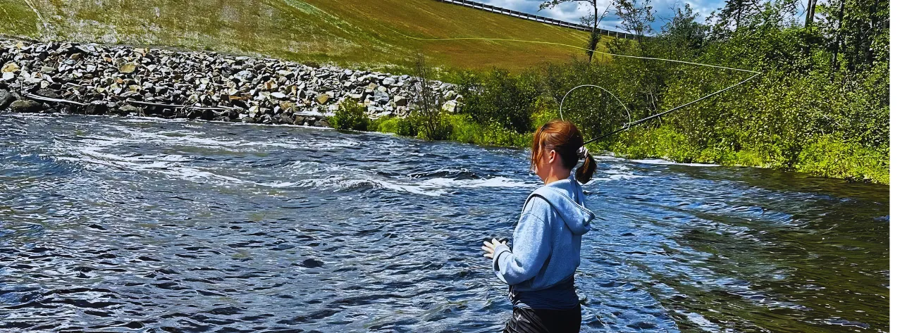 Fly angler casting while wading a fast, clear Maine river on a bright summer day